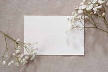 Blank Paper Card And Gypsophila Flowers On Neutral Beige Linen Texture Background, Aesthetic Floral Greeting Card Or Wedding Invitation Template With Copy Space