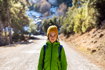 Wall Mural - A boy with a backpack in the middle of a forest road, a child is exploring wildlife, a child is standing alone among the trees. Travel and hiking.