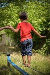 Wall Mural - young boy walking on a wire with the help of a woman coach