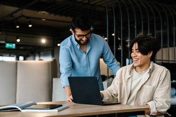 Two male colleagues working together on laptop computer in office