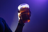 Fototapeta Mapy - Person holding a plastic cup of beer in the nightclub.