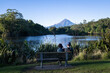 © Janice - Couple sitting on the bench and enjoying the view of Mt Taranaki at Lake Mangamahoe. New Plymouth.