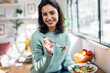 © nenetus - Beautiful smiling woman eating healthy salad while sitting on the table at home.