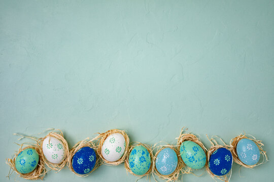 Fototapete - Row of hand painted Easter eggs on light green concrete background. Flat lay, top view with copy space