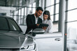 © standret - Showing information in the graphic tablet. Man in formal clothes is consulting woman about the automobile in the car dealership