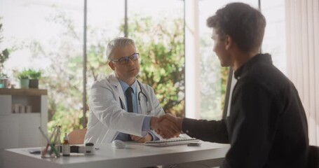 Wall Mural - Caucasian Doctor Speaking to a Young Man During a Consultation in Health Clinic. Physician in White Lab Coat Shaking Hands with Patient After Agreeing on Suggested Clinical Treatment. Slow Motion