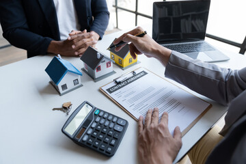 Two young Asian businessmen or architects are describing architectural house model in their office together for the construction of  housing estate project in  prime location the location is perfect