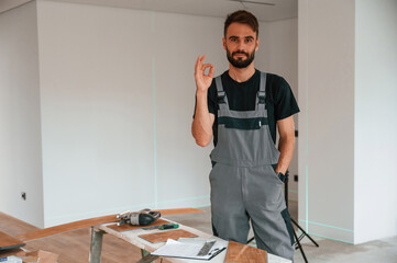 Wall Mural - Standing, showing okay gesture. Man is installing new laminated wooden floor