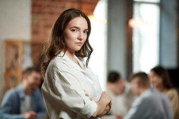 Project manager. Serious ambitious young woman in formal wear attentively looking at camera. Blurred employees on background in office. Concept of business, teamwork, career development, brainstorming