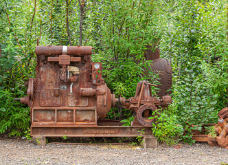 Fox, Alaska, USA - July 26, 2011: Eldorado Gold Mine museum and park. Old rusted-metal, heavy steam disperser machine as used in placer mining set against green tree backdrop