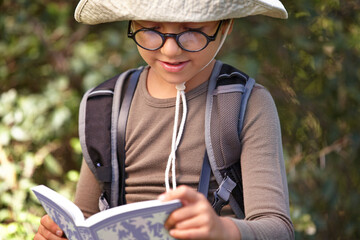 Reading and nature are his two favourite things. a young kid reading a book outdoors.