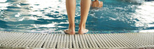 Banner. Women's Feet On The Step At The Entrance To The Fiberglass Pool With Blue Water In The Spa Area Of The Resort. White Wooden Flooring Made Of Teak Or Larch Board. High Quality Photo