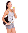 Its almost time for my latest weigh-in. Portrait if a sporty young woman holding a scale while eating an apple.