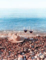 Wall Mural - Two glasses with red wine and a straw hat on the shore in 