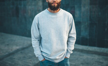 City Portrait Of Handsome Hipster Guy With Beard Wearing Gray Blank Hoodie Or Hoody And Hat With Space For Your Logo Or Design. Mockup For Print