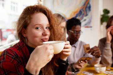 Multiethnic company of young people drinking coffee and playing games, looking at smartphones, taking selfies.