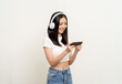 © Chanakon - Beautiful young asian women play mobile game and put on wireless headphone standing on isolated background. Playing game on smartphone winning victory moment. Very enjoy and fun relax time