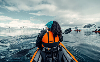 Female Kayaker Paddling Through Calm Water Of Antarctica with Beautiful Moody Snowy landscape With A Group of Other kayakers