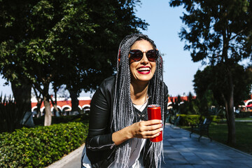 Young latin woman with braids hair holding beverage drink soda can on the street in Mexico, hispanic people