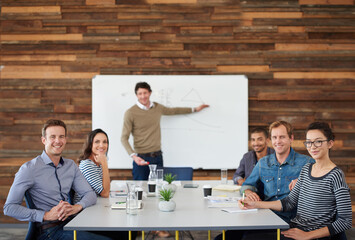 Poster - Our brand is trending. Portrait of a group of coworkers sitting at a conference table during a presentation.