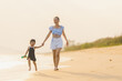 © etemwanich - happy time of mom and daughter in dress black walking and run play on the beach with blur background beautiful sunset light in the sea