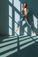 Wall Mural - Asian dancer girl makes an acrobatic jump illuminated by the sun that enters through the window in an empty building. isolated