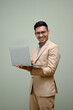 © bongkarn - Successful Asian businessman holding his laptop, standing against green studio background.