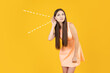 Eavesdropping on secrets and conversations concept with young woman puts her hand to her ear and eavesdrops on yellow background.