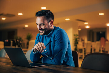 Smiling man working over the laptop, holding glasses.