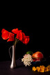 Still life on a black background. A bouquet of wild red poppies in a flacon. Bowl with fruits - pomegranate, apple and avocado. Copy space.