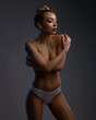 © oleg_ermak - A beautiful half-naked woman covering chest with hands. Topless blonde model in white seamless panties covering breast by arms on a gray studio background.