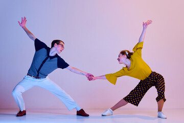 Wall Mural - Having fun. Young man and woman in stylish clothes dancing retro dance against gradient pink purple studio background. Concept of art, retro style, hobby, party, fun, movements, 60s, 70s culture