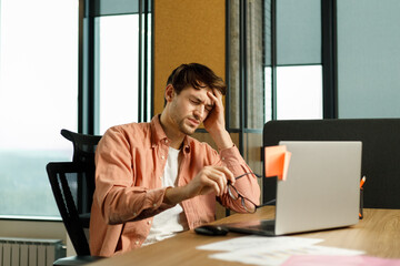 Wall Mural - Stress and headache at work. A young businessman is sitting in the office, holding his head