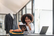© wichayada - Portrait of young female tailor with tape measure in her neck sitting in stylish dress and holding digital tablet in office
