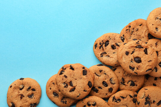 Wall Mural - Many delicious chocolate chip cookies on light blue background, flat lay. Space for text