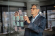 © JustLife - Portrait of successful businessman in office. Man writing ideas on colorful stickers on glass wall