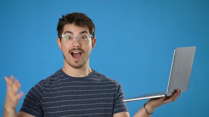 Wall Mural - Young smiling happy man 20s in striped t-shirt hold use work on laptop pc computer browsing chatting surfing internet isolated on plain blue background studio portrait. People lifestyle concept