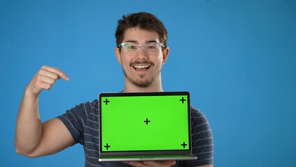 Wall Mural - Young smiling happy man 20s wear striped t-shirt hold use laptop pc computer with tracking points green screen, browsing chatting with blank screen workspace area isolated on solid blue background