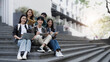 © wichayada - Group of cheerful Asian college students sitting on stairs, showing fists, celebrating triumph