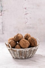 Sticker - Raw walnuts in shell inside a wicker basket on white background, vertical shot