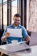 © kerkezz - Satisfied young man with glasses sitting at a desk and doing paperwork at his workplace.