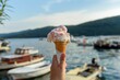 Selective focus shot of a hand holding an ice cream in a cone with moored boats in the sea