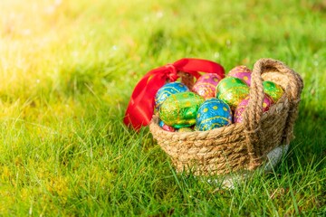 Wall Mural - Easter eggs in basket in fresh green grass. Easter season banner with green nature bokeh background. Colorful decorated eggs in wicker basket. Spring season decoration for web banner