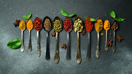 Wall Mural - A set of colored spices in metal spoons. On a black slate background. Top view.