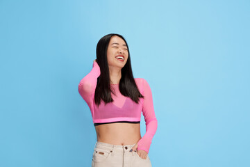 Poster - Portrait of young beautiful korean girl smiling, laughing, posing in colorful top against blue studio background. Concept of emotions, facial expression, fashion, youth, lifestyle. Ad