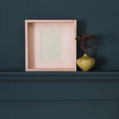 Wall Mural - Square picture frame and minimal round vase with a decorative twig against dark blue wall from panels.	