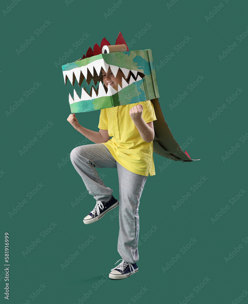 Little boy in cardboard dinosaur costume on green background