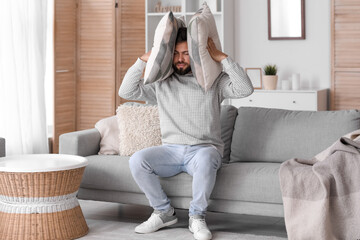 Wall Mural - Young man with pillows suffering from loud noise at home