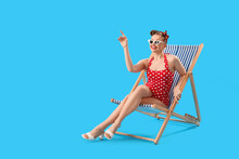 Young Pin-up Woman Sitting In Deck Chair On Blue Background