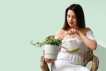 Canvas Print - Young woman watering houseplant in armchair near green wall